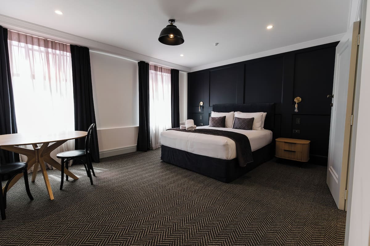 Una habitación de hotel con una cama grande, un escritorio con sillas y una pequeña mesita de madera.