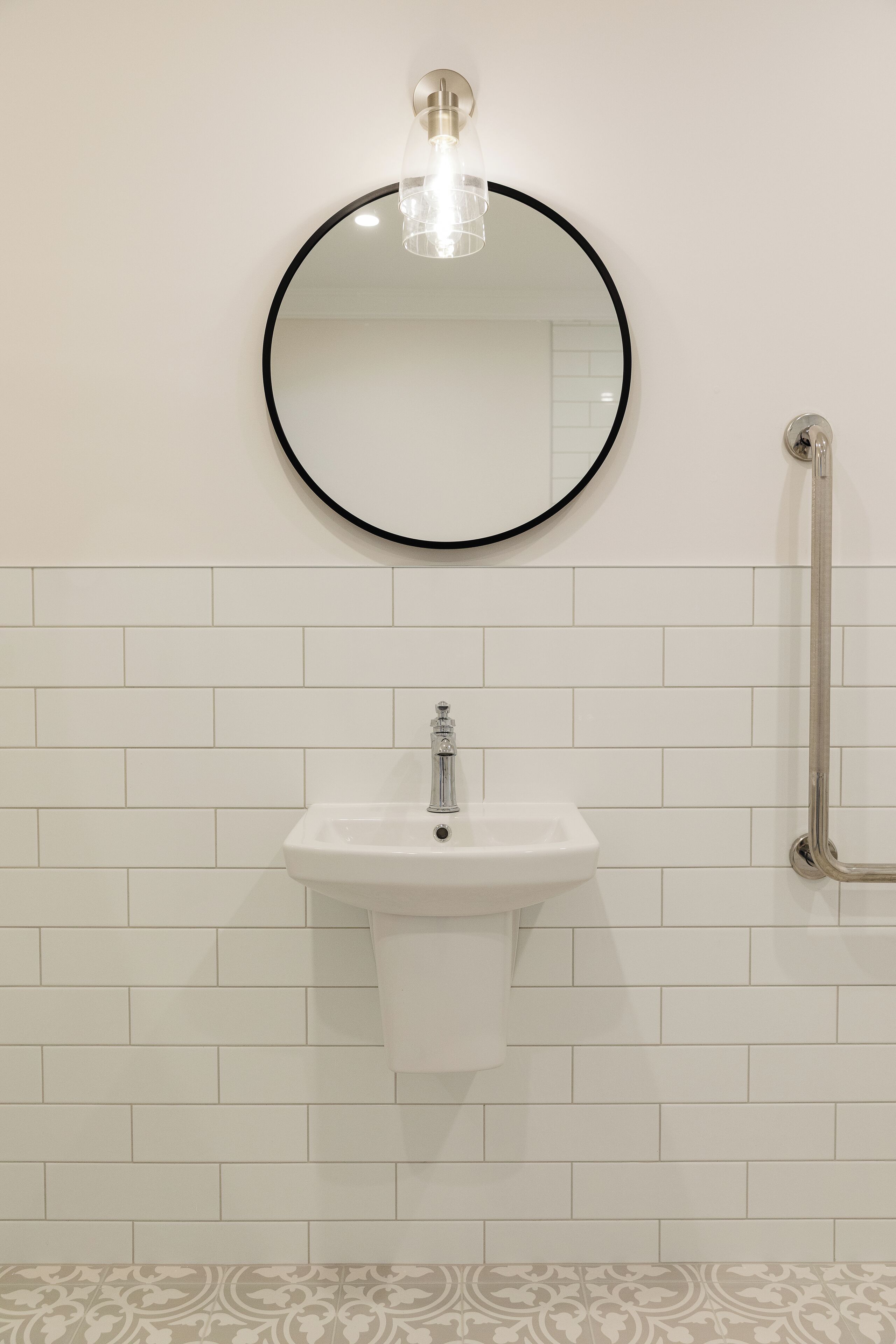 A bathroom with a round mirror, a white sink, and a handrail.