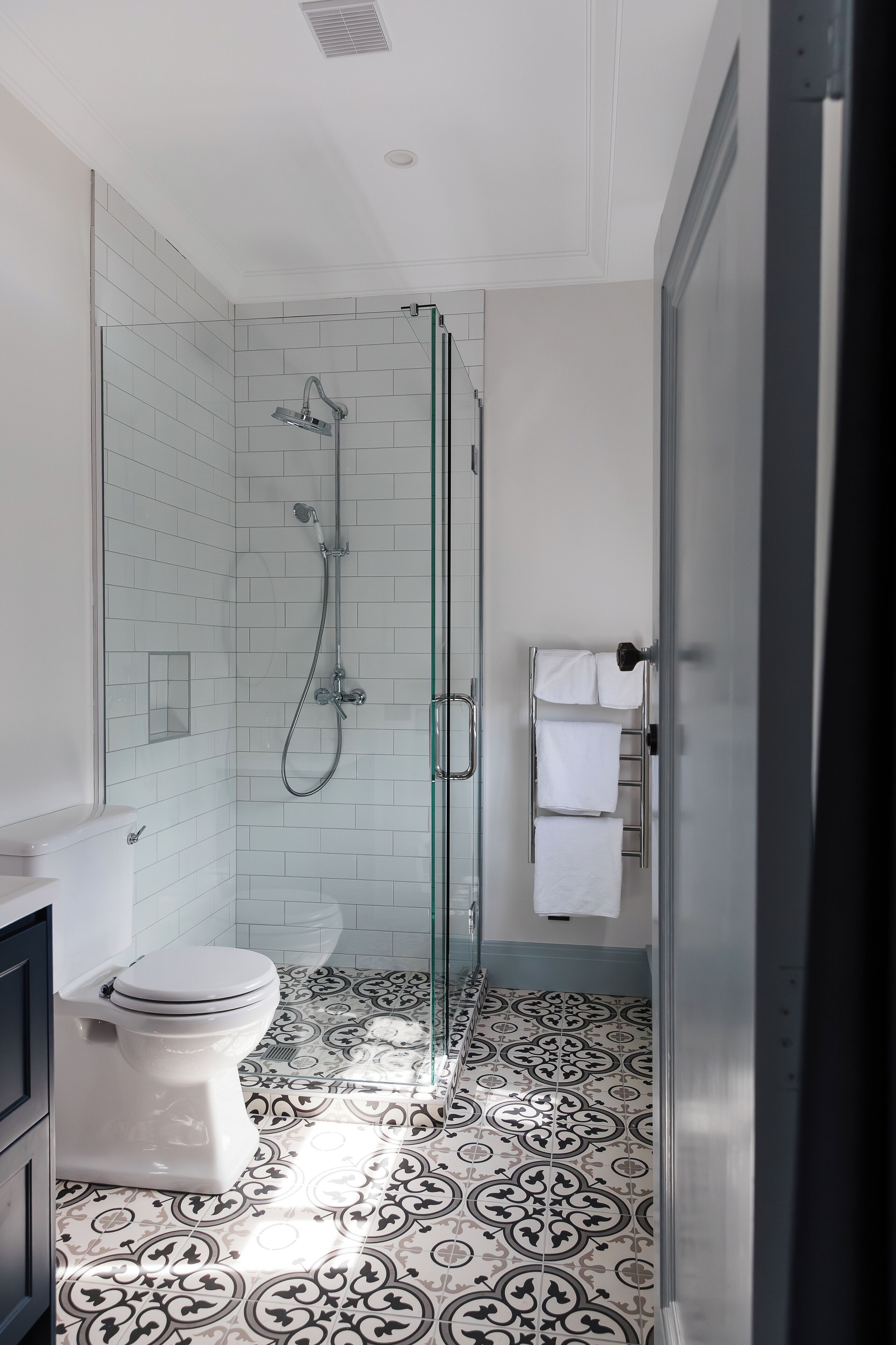 Een moderne badkamer met een glazen douchecabine, een toilet en een vloer met een patroon.