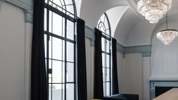 A spacious room with a large window, a chandelier, a wooden table, and a blue sofa. - Criterion Hotel Napier (Napier)