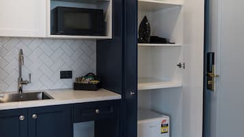 Cocina compacta con armarios blancos, microondas y un refrigerador pequeño.