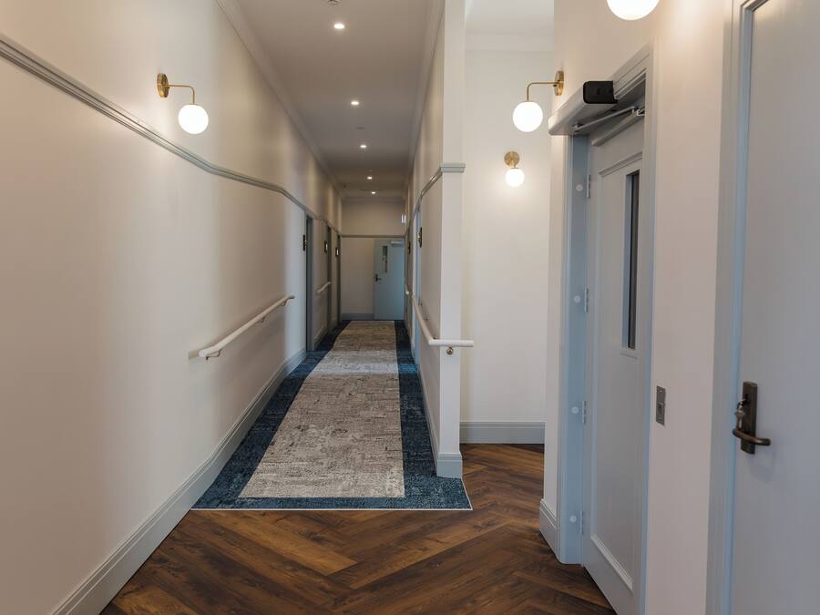A hallway with a wooden floor, a blue and white rug, white walls, and doors with light blue trim.