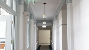 A hallway with white walls, wooden flooring, and a chandelier. - Criterion Hotel Napier (Napier)