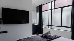 A hotel room with a bed, a flat-screen TV mounted on the wall, a window with curtains, and a view of the outside. - Criterion Hotel Napier (Napier)