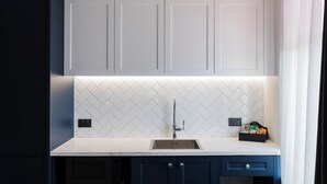 A modern kitchen with white herringbone backsplash, a stainless steel sink, and dark blue cabinets. - Criterion Hotel Napier (Napier)
