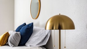 Un dormitorio ordenado con una cama, una mesita de noche con lámpara, un espejo en la pared y un revestimiento texturizado.