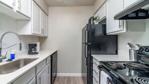 Una cocina compacta con armarios blancos, un refrigerador negro, una estufa y una cafetera.