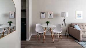 Una sala de estar moderna con una mesa de comedor redonda, sillas blancas, un sofá beige y una lámpara de pie.