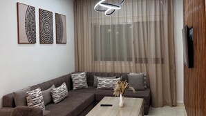 A modern living room with a sectional sofa, a coffee table, and a TV mounted on the wall. - Belmar Martil - Chic and close to the sea (Martil)
