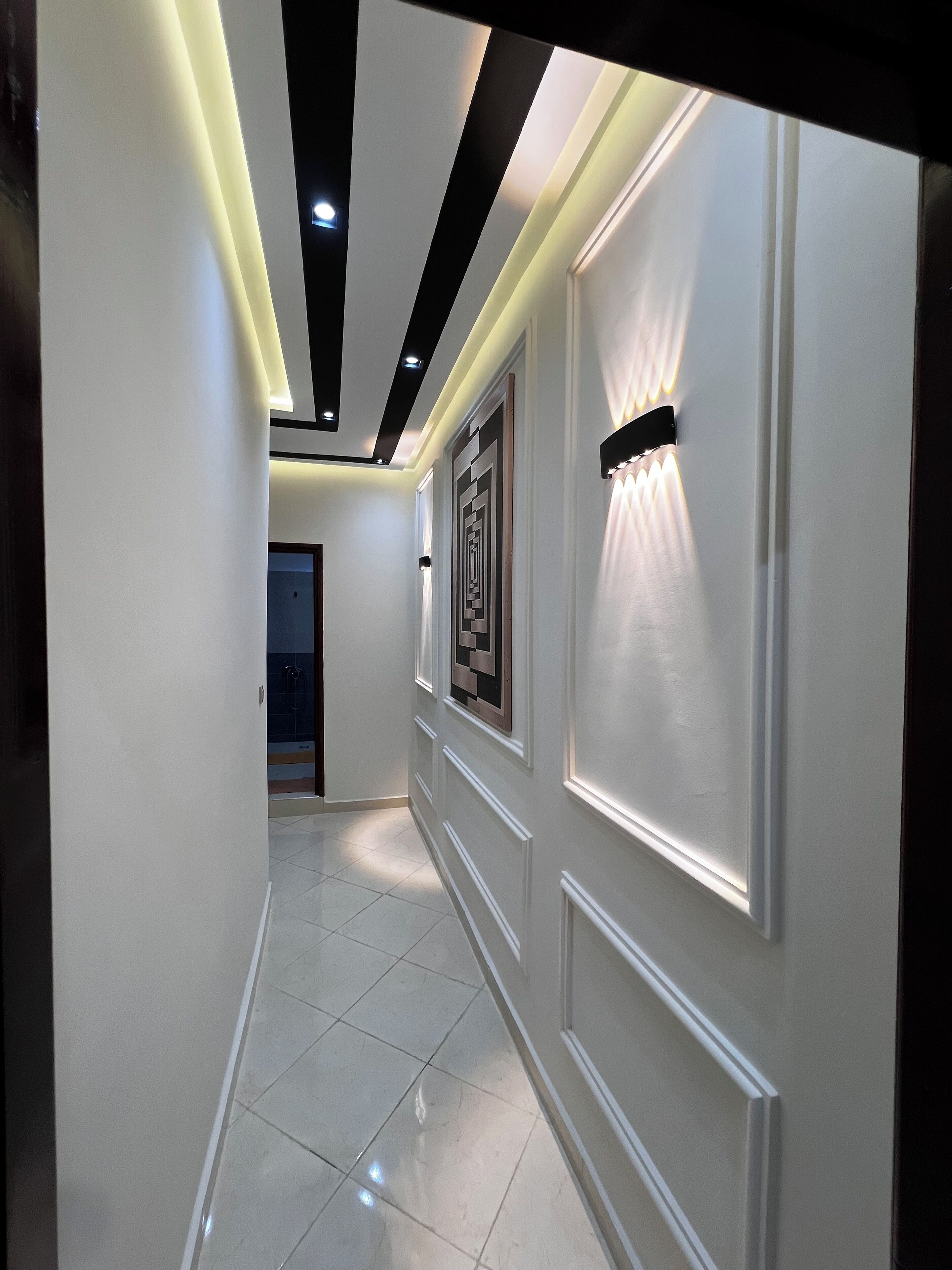 A hallway with white walls, a tiled floor, and recessed lighting.