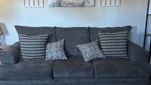 A grey sofa with patterned cushions, a framed abstract painting, and a geometric rug.