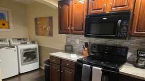 A kitchen with wooden cabinets, a microwave, an oven, a stove, and a washing machine.
