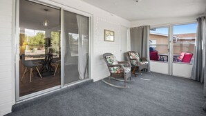 Ein Balkon mit einer Schiebeglastür, Rattan-Schaukelstühlen und einem Tisch mit Stühlen.