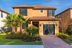 A two-story house with a tiled roof, a garage, and a well-maintained lawn with palm trees. - Solterra Resort, Elegant 5 bdrm home with Pvt pool (Davenport)