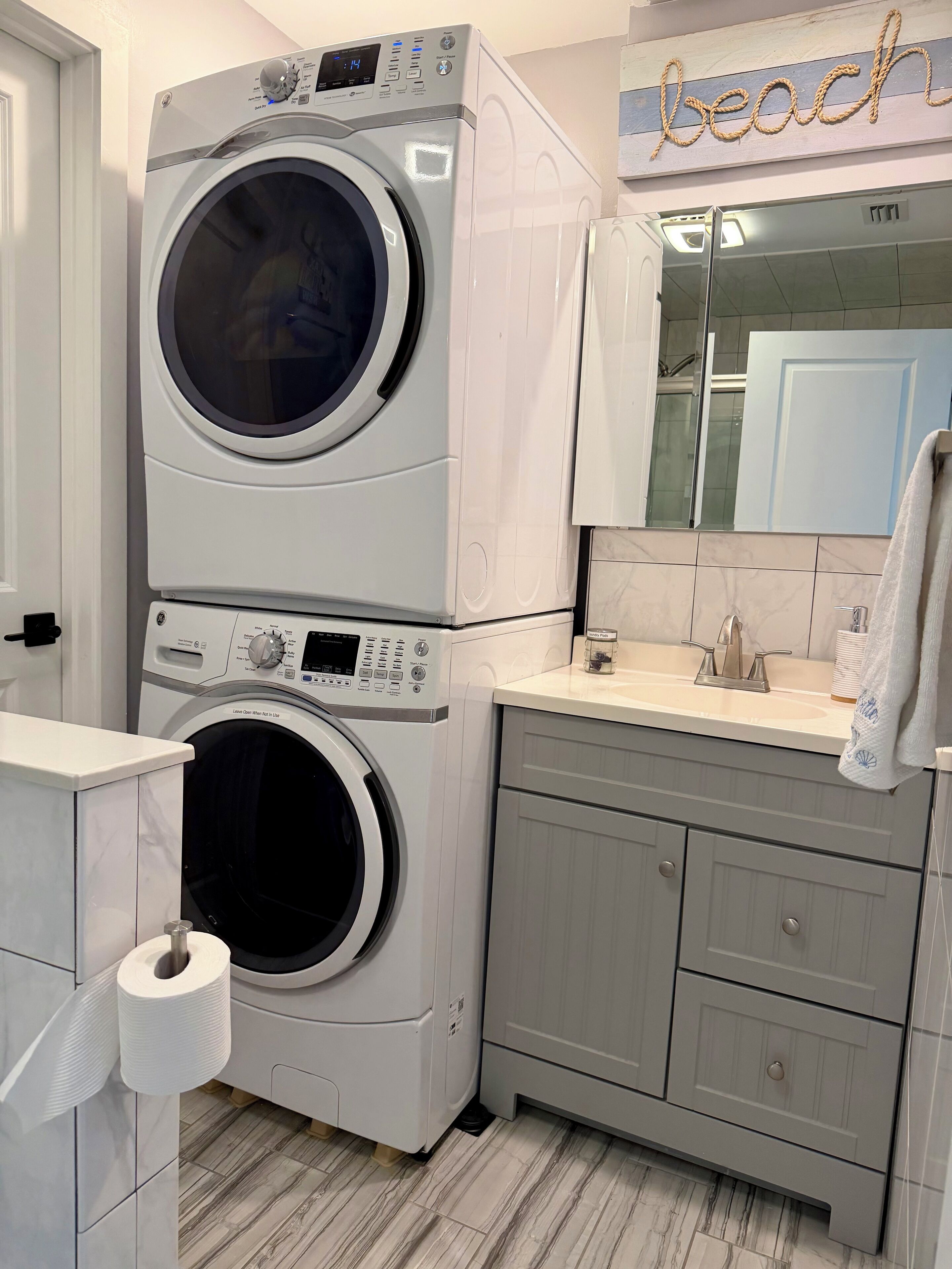 A compact laundry area with stacked washing machines, a sink, and a mirror.