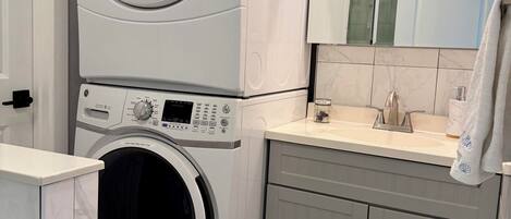 A compact laundry area with stacked washing machines, a sink, and a mirror.
