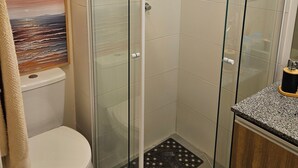 Een douchecabine met glazen wanden, een handdouche, een toilet en een ingelijste foto aan de muur.