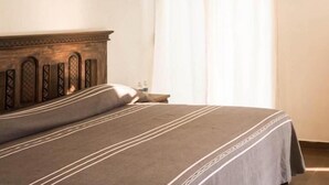 A bedroom with a wooden headboard, a bed with striped bedding, a nightstand, and a window with sheer curtains.