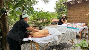 A massage therapy session in an outdoor setting with a brick wall and trees in the background.