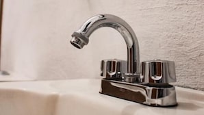 A bathroom sink with a chrome faucet and a glass soap dispenser on the wall.