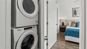 Ein Waschraum mit zwei Whirlpool-Waschmaschinen und ein Schlafzimmer mit Bett, Nachttisch, Lampe sowie Kunstwerk an der Wand.