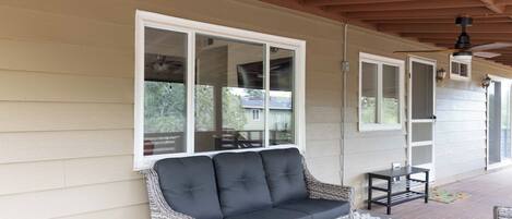 A covered porch with a wicker sofa, a glass coffee table, and a small table.