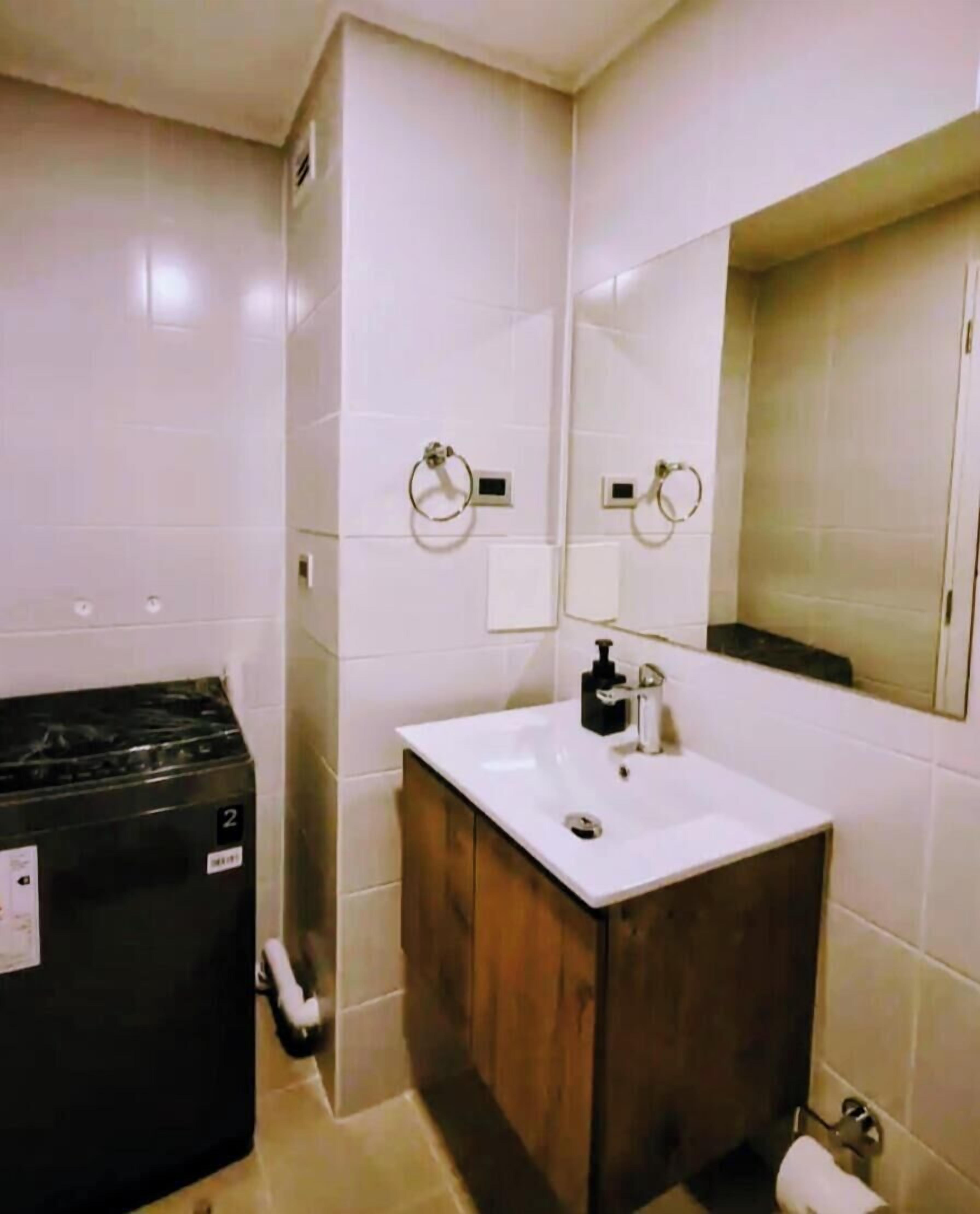 A small bathroom with a white sink, a mirror, and a black washing machine.