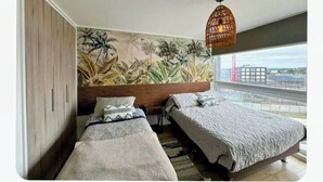 Une chambre avec deux lits, une grande fenêtre et une fresque représentant une végétation tropicale.