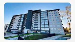 Un immeuble résidentiel moderne à plusieurs étages, doté de balcons, d’une piscine et d’une pelouse bien entretenue.