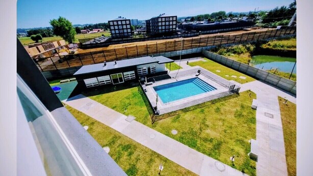 Vue aérienne d’un quartier résidentiel avec une piscine, des bâtiments modernes et un terrain de sport clôturé.