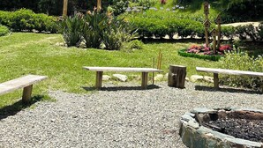 Un jardín con un gazebo de madera, bancos y una construcción rústica.