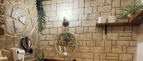 A bathroom with a stone wall, wooden bench, sink, toilet, and a mirror.