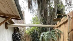 Un patio con suelo de piedra y una pérgola de madera, rodeado por una valla de madera y diversas plantas.