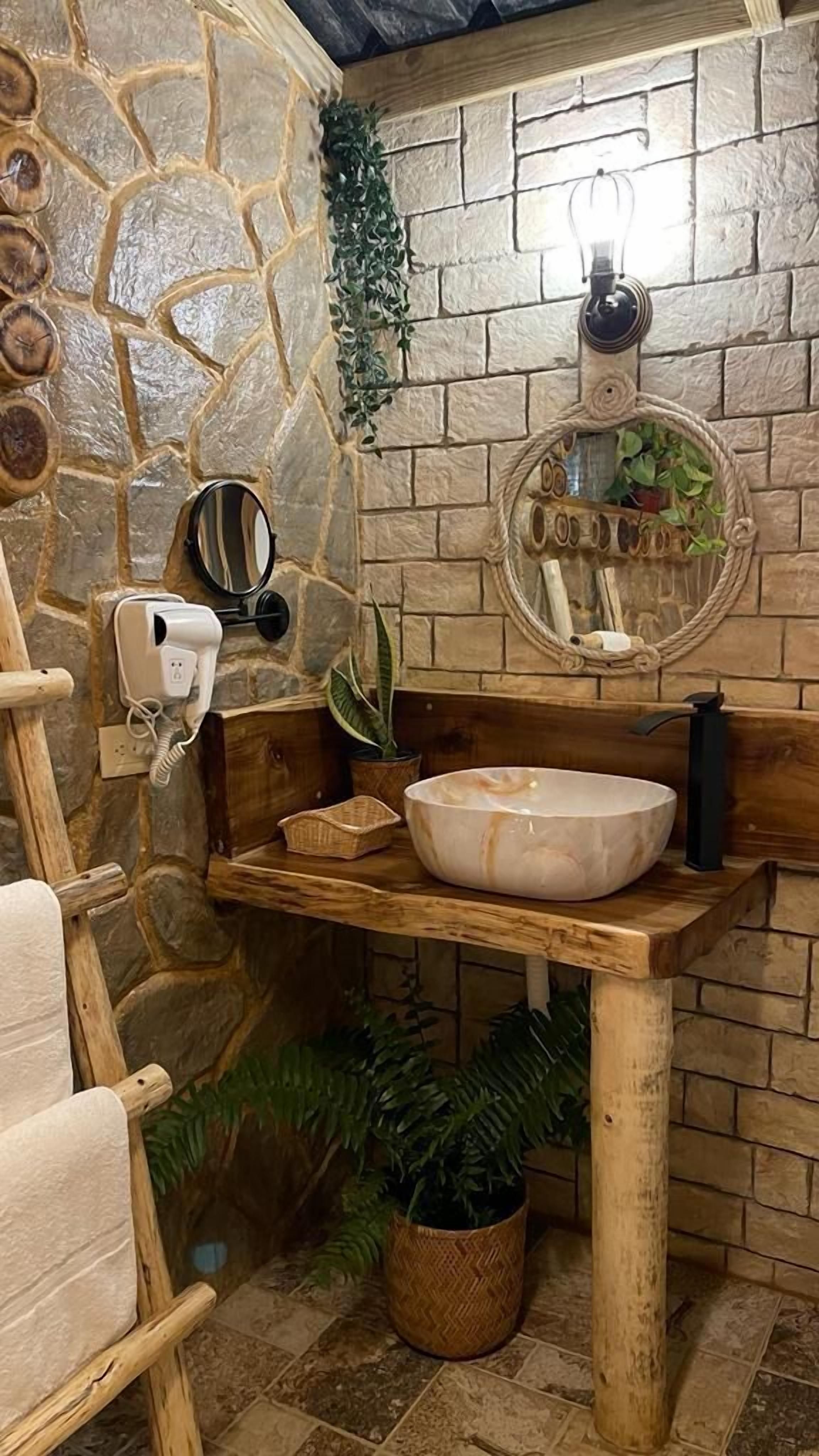 A bathroom with a stone wall, wooden vanity, a large mirror, a sink, and a towel rack.