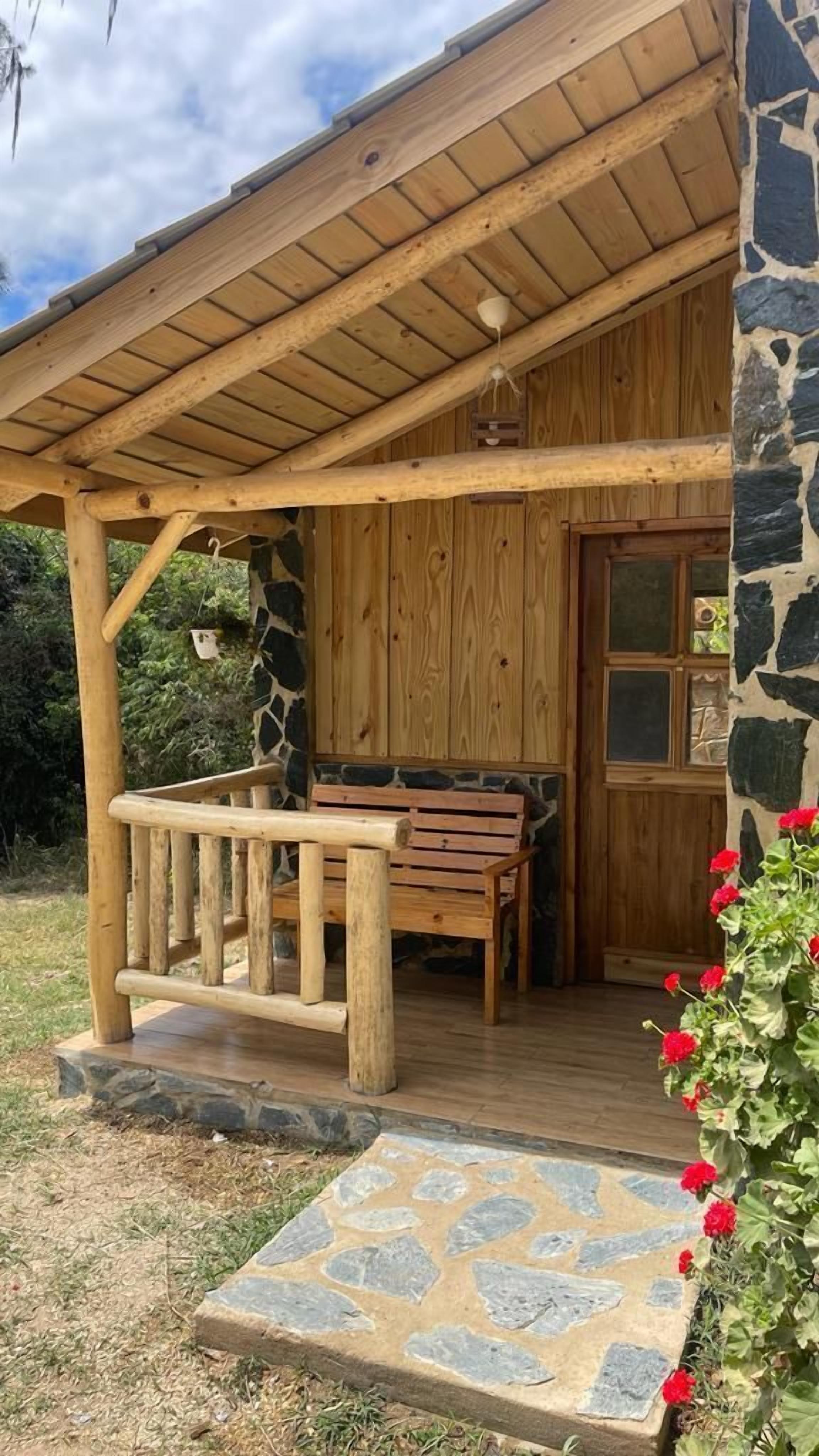 A wooden cabin with a stone exterior, a porch with a bench, and a stone pathway leading to the entrance.
