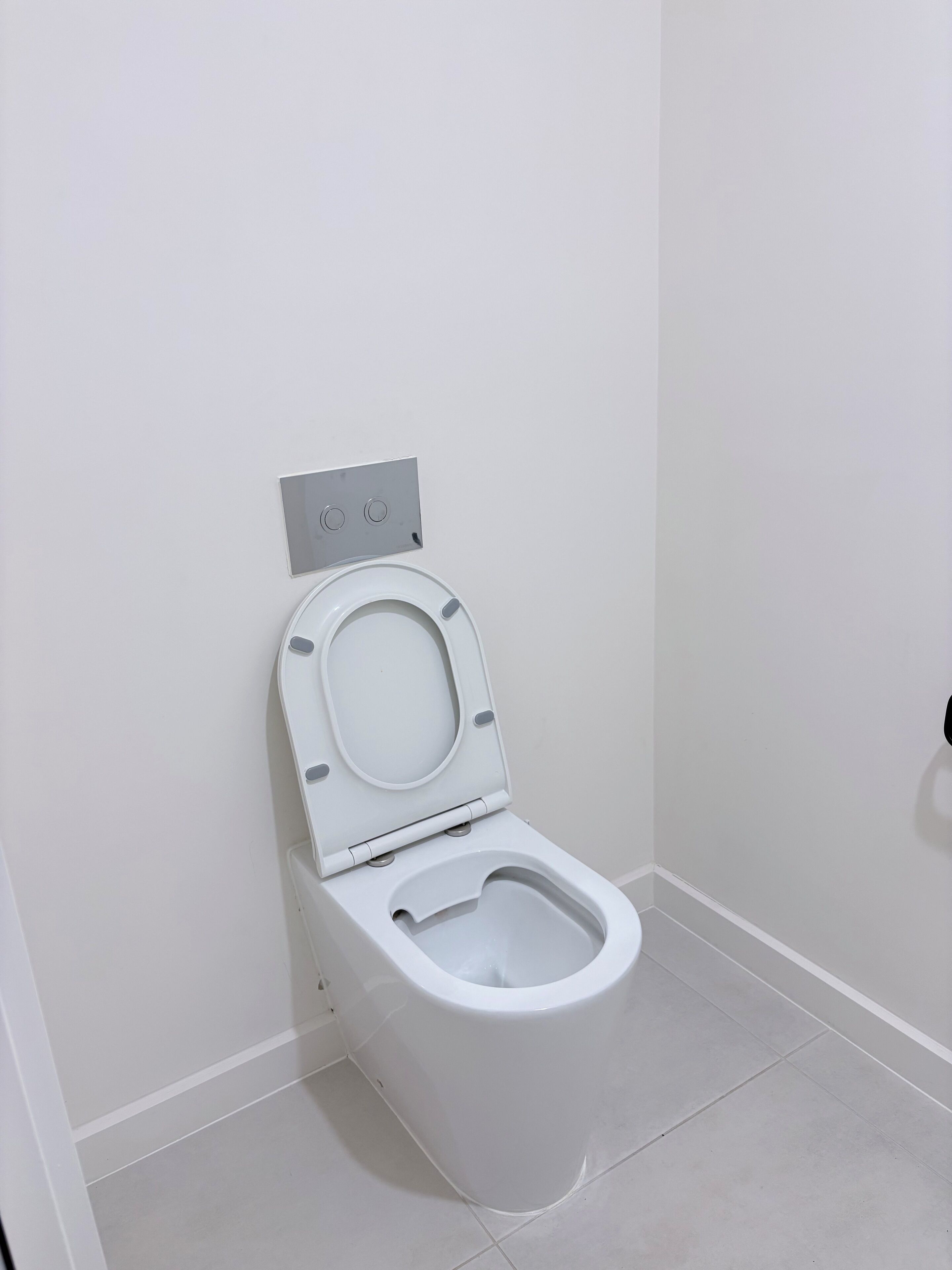 A white toilet with a closed lid in a bathroom with white walls and tiled floor.