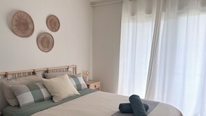Una cama bien hecha con una almohada de cuadros, una toalla enrollada y una lámpara de noche.
