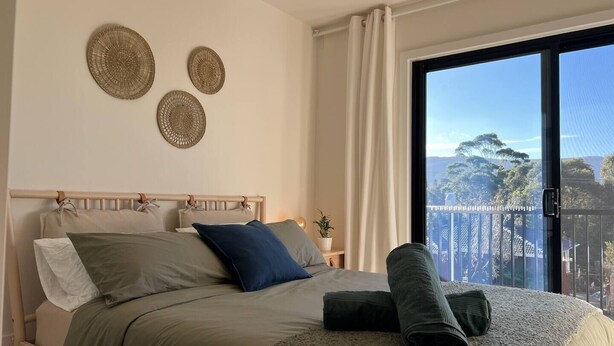 Un dormitorio con cama, almohadas, una colcha y vistas al exterior a través de un ventanal grande.