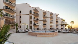 Un hotel con varios balcones, una zona de piscina central con sillones de descanso y palmeras.