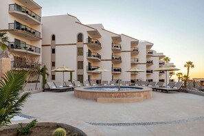A hotel with multiple balconies, a central pool area with lounge chairs, and palm trees. - SPRING BREAK! Fabulous Ocean Front 2-Bed 3-Bath Luxury Medano Beach Resort (Cabo San Lucas)