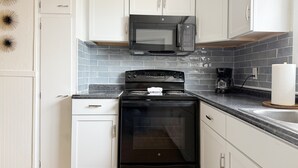 Una cocina con armarios blancos, una estufa negra, un microondas y una cafetera.