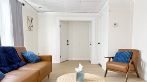 Una sala de estar moderna con un sofá de cuero marrón, un sillón azul y una mesa de centro redonda de madera con un dispensador de pañuelos.