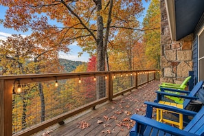 A wooden deck with a railing, outdoor seating, and a view of autumn foliage. - FreeDollywoodTix+Pool+Secluded+Modern+HotTub (Sevierville)