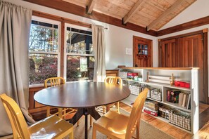 A dining area with a round table and chairs, a bookshelf with storage bins, and a view of trees through large windows. - FreeDollywoodTix+Pool+Secluded+Modern+HotTub (Sevierville)