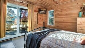 Camera da letto in una baita di legno con un letto, una cassettiera, una TV e una finestra vista foresta.