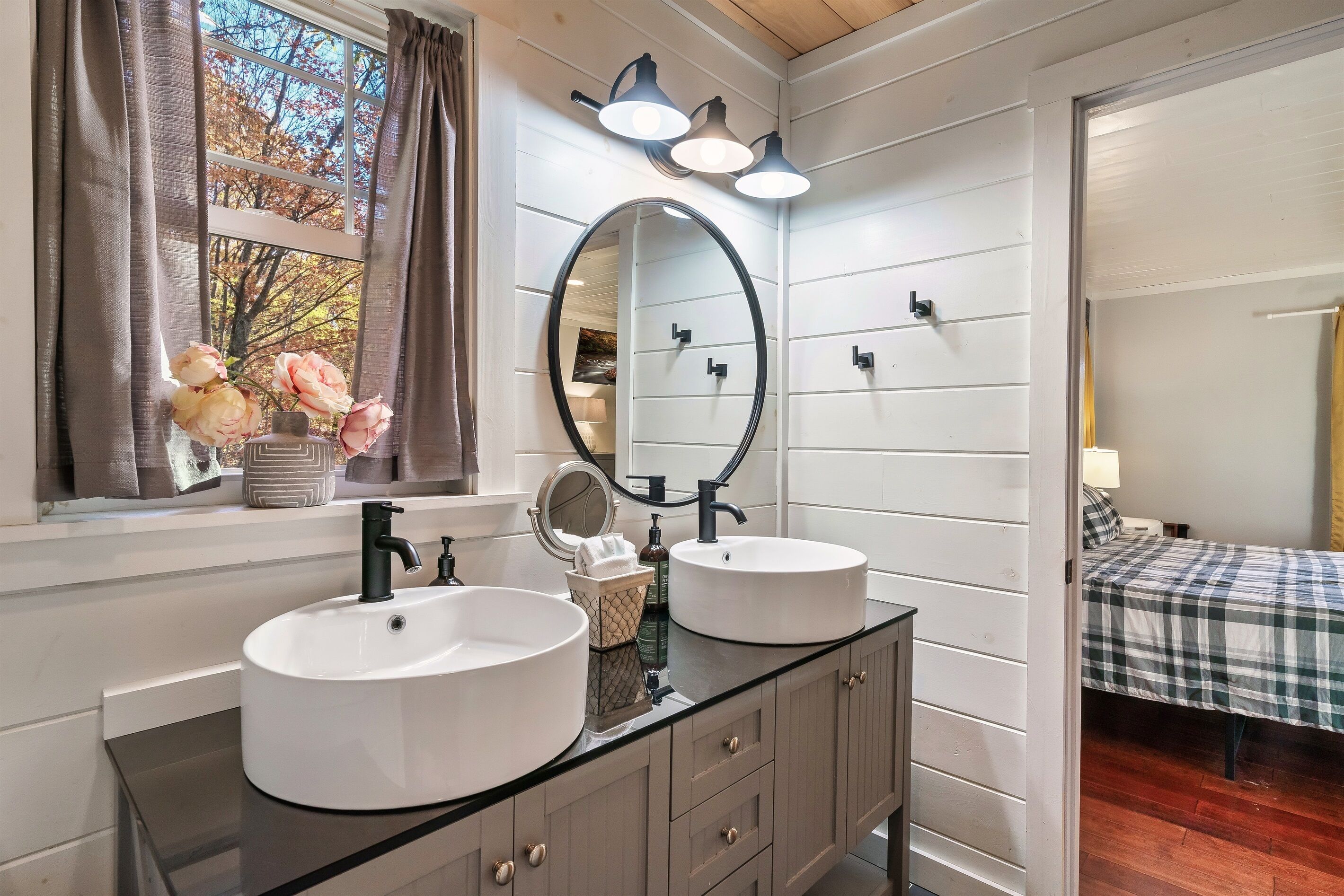 A bathroom with two sinks, a large mirror, and a window with curtains.