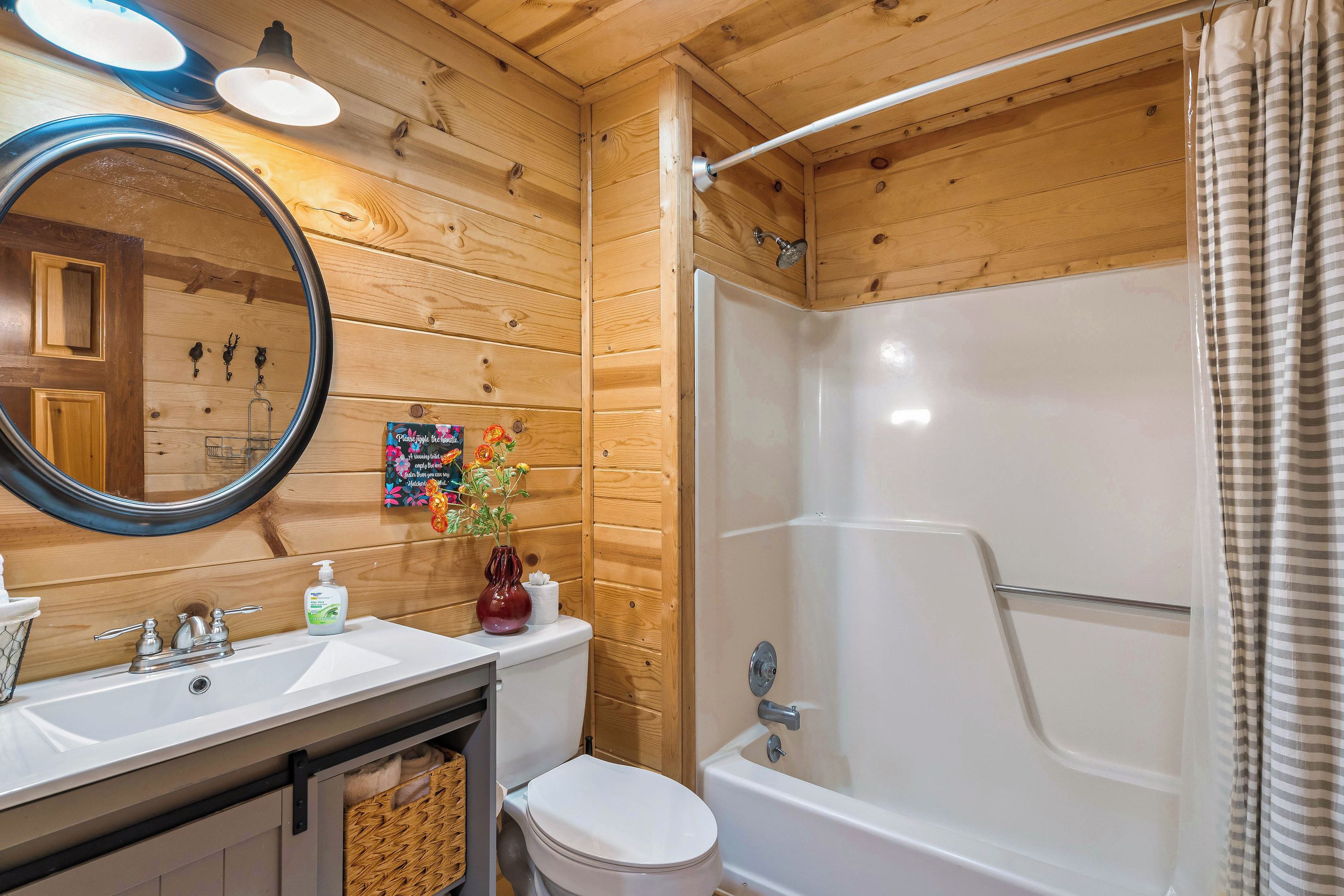 A wooden interior bathroom with a sink, mirror, toilet, and shower.