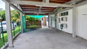 Un espacio al aire libre techado con suelo de hormigón, un banco de madera y unidades de aire acondicionado en la pared.