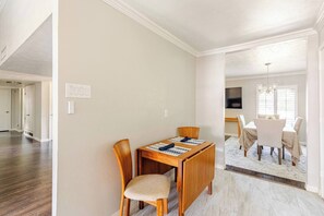 A dining area with a wooden table and chairs, a chandelier, and a TV mounted on the wall. - Dallas Home for Extended Stays: 3BR, Pool, Workspace and Garage (Dallas)