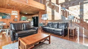 A spacious living area with a wooden staircase, two leather sofas, a coffee table, and a television. - Free Dollywood Tickets, Sauna, Hot Tub, Secluded Modern Cabin, Dogs OK (Sevierville)